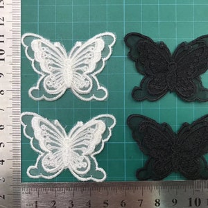 May include: Two pairs of butterfly-shaped fabric appliques. One pair is white and the other is black. The appliques are made of a sheer fabric with a delicate lace design.