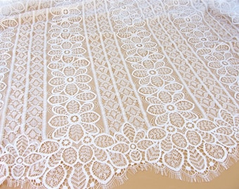 May include: White lace fabric with a delicate floral pattern. The lace has a vertical striped design with a scalloped edge.