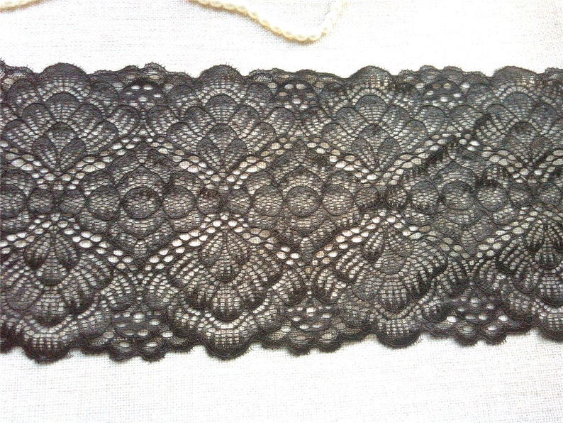 Pode incluir: Close-up de uma renda preta com borda ondulada. A renda apresenta um padr&atilde;o floral repetido com trabalho aberto detalhado. Ideal para costura, artesanato ou para adicionar elementos decorativos a roupas ou projetos de decora&ccedil;&atilde;o.