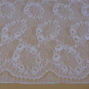 May include: White lace fabric with a delicate floral pattern. The lace has a scalloped edge and a soft, flowing texture.