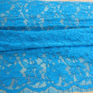 May include: Turquoise blue lace fabric with a floral pattern. The lace has a scalloped edge.