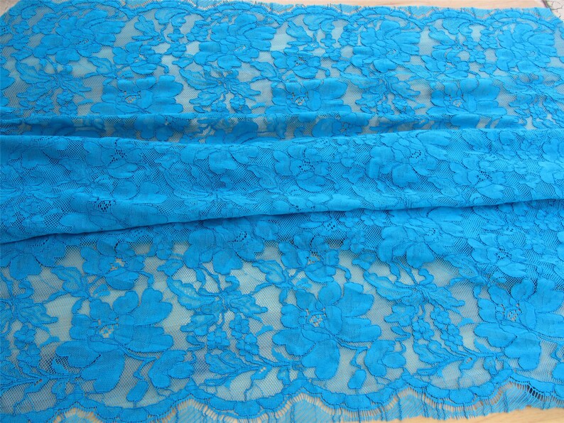 May include: Turquoise blue lace fabric with a floral pattern. The lace has a scalloped edge.