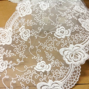 May include: White floral lace trim with a delicate pattern of roses and leaves. The lace is sheer and has a soft, romantic feel.