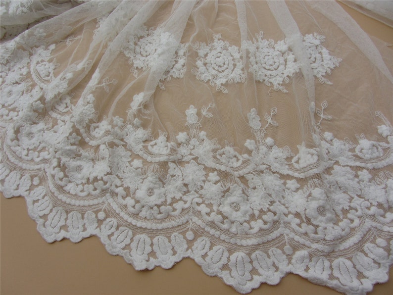 Pu&ograve; includere: Tessuto di pizzo bianco con un delicato motivo floreale. Il pizzo ha un bordo a festoni ed &egrave; perfetto per aggiungere un tocco di eleganza a qualsiasi progetto.