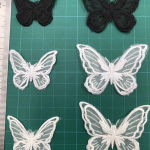 May include: Four white and two black butterfly appliques. The appliques are made of lace and have a delicate, intricate design. They are perfect for adding a touch of elegance to any project.