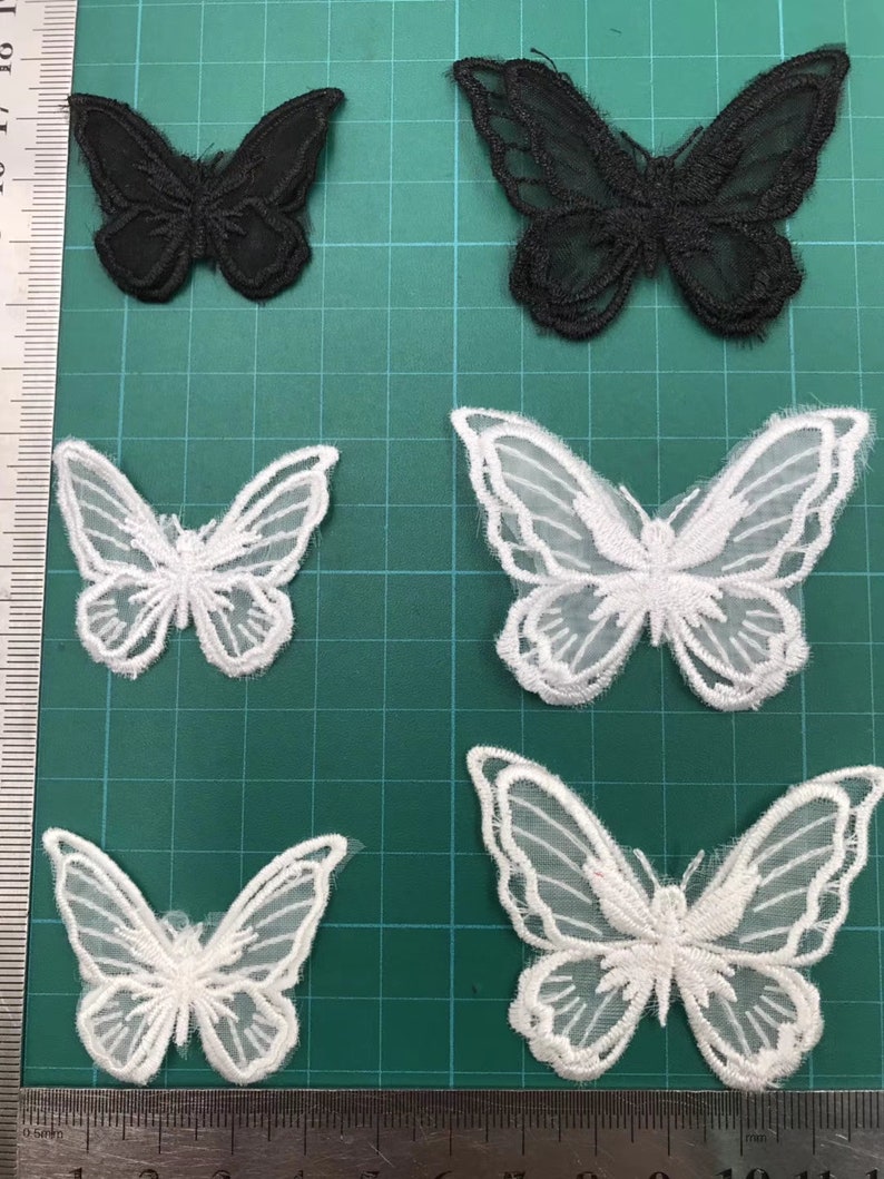 May include: Four white and two black butterfly appliques. The appliques are made of lace and have a delicate, intricate design. They are perfect for adding a touch of elegance to any project.