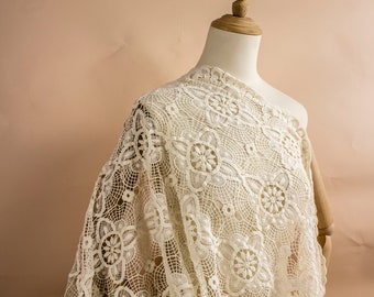 May include: White crochet fabric with a delicate floral pattern. The fabric is draped over a dress form.