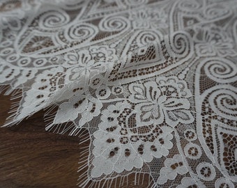 May include: White lace fabric with a delicate floral and swirl pattern. The lace has a scalloped edge.
