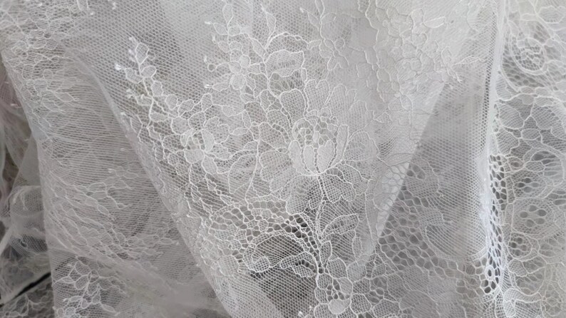 May include: White lace fabric with a floral pattern. The lace is delicate and intricate, with a soft, flowing texture.