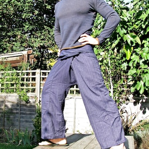 May include: A person wearing a gray long-sleeved shirt and dark blue striped pants with a wrap-around style. The pants are tied at the waist with a brown fabric belt.