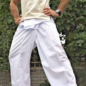 May include: White cotton trousers with a wrap-around style, worn by a person standing on a wooden deck.