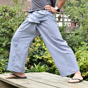 May include: A person wearing a pair of light blue striped pants with a loose, flowing fit. The pants are tied at the waist with a fabric sash. The person is standing on a wooden platform with their feet slightly apart.