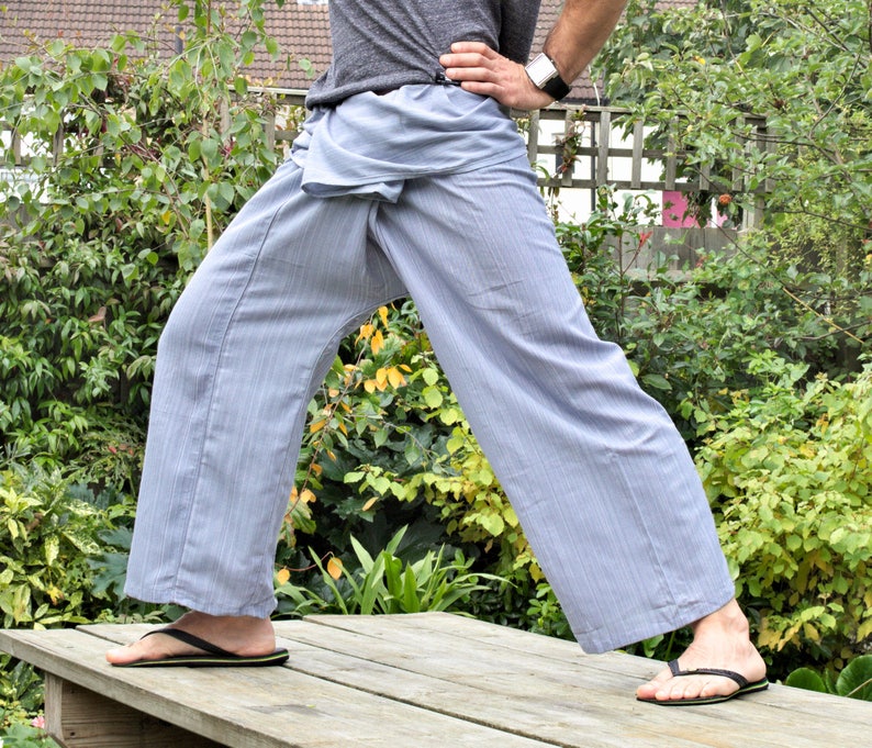 May include: A person wearing a pair of light blue striped pants with a loose, flowing fit. The pants are tied at the waist with a fabric sash. The person is standing on a wooden platform with their feet slightly apart.