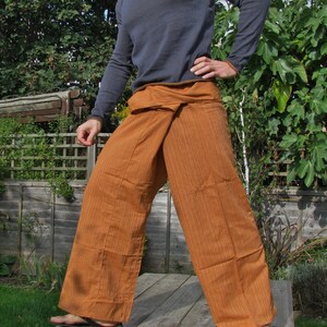 May include: A person wearing a brown and orange striped wrap pants with a dark blue long-sleeved shirt. The pants are tied at the waist and have a loose, flowing fit.