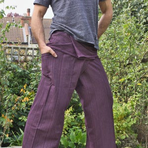 May include: A person wearing a pair of purple striped pants with a grey t-shirt. The pants have a unique wrap-around style and are made of a soft, comfortable fabric.