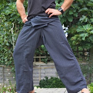 May include: A person wearing a gray striped pants with a black and gray striped pattern. The pants are tied at the waist with a sash. The person is standing on a wooden deck.