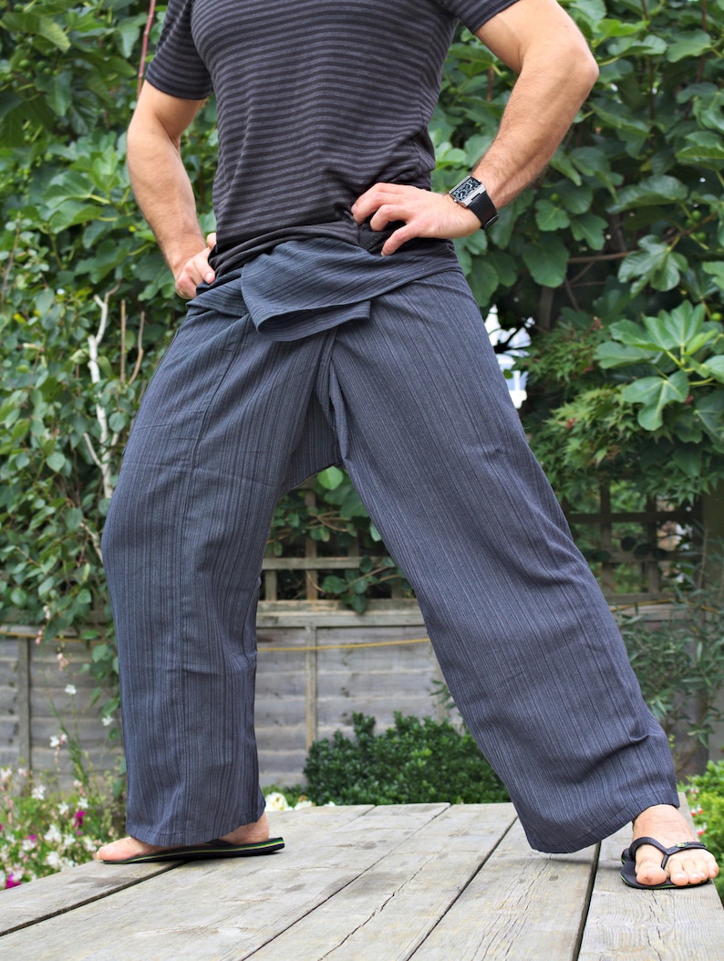 May include: A person wearing a gray striped pants with a black and gray striped pattern. The pants are tied at the waist with a sash. The person is standing on a wooden deck.