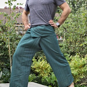 May include: A person wearing a gray t-shirt and green striped pants. The pants are tied at the waist with a fabric sash. The person is standing on a wooden platform.