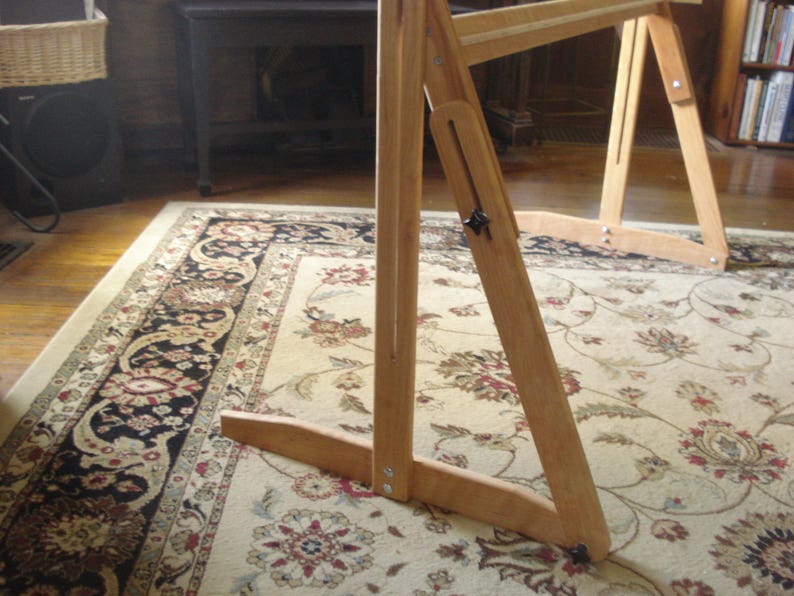 May include: A wooden frame with adjustable legs, standing on a patterned rug. The frame is made of light wood and has a simple design.