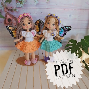 May include: Two crocheted dolls with butterfly wings. The dolls are wearing floral headbands and colourful dresses. The dolls are standing on a wooden surface. The text "ENGLISH PDF PATTERN" is visible in the image.