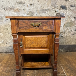 May include: A wooden side table with a drawer and a cabinet door. The table has a shelf underneath and decorative legs. The table is made of dark wood with a natural finish.