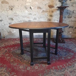 May include: A round wooden table with a dark brown tabletop and black legs. The table is set on a patterned red rug. A bust on a pedestal is visible in the background.