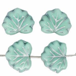 May include: Four pale green leaf-shaped beads with silver veins and edges. Two are strung on a silver wire. The beads have a matte finish against a white background. Each bead is approximately 1.5 cm wide.