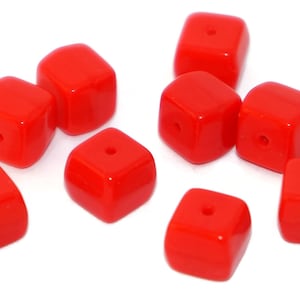 Puede incluir: Diez cuentas cuadradas de vidrio rojo brillante con un agujero en el centro de cada cuenta.