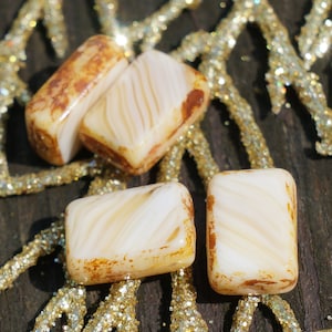 Peut inclure: Quatre carreaux de verre blanc et brun avec un motif marbré. Les carreaux sont disposés en quinconce sur un fond doré.