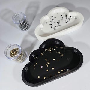 May include: Two cloud-shaped trays, one white and one black, each filled with small, decorative gems. Two clear plastic containers filled with similar gems are also present. The trays are likely used for organizing small items.