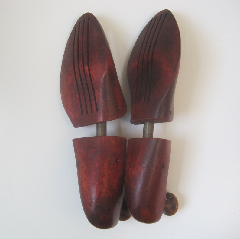 Puede incluir: Un par de hormas de zapatos de madera con un acabado marr&oacute;n rojizo. Las hormas tienen una parte superior redondeada y una varilla de metal que se extiende por el centro.