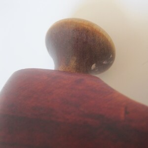 Puede incluir: Primer plano de un pomo de madera con un acabado marr&oacute;n oscuro. El pomo es redondo y tiene una superficie lisa. El pomo est&aacute; unido a un objeto de madera m&aacute;s grande.