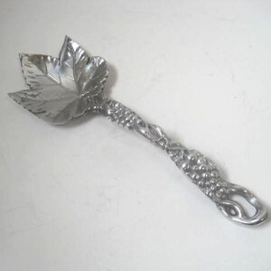 May include: A silver serving spoon with a leaf-shaped bowl and a handle shaped like a grapevine.