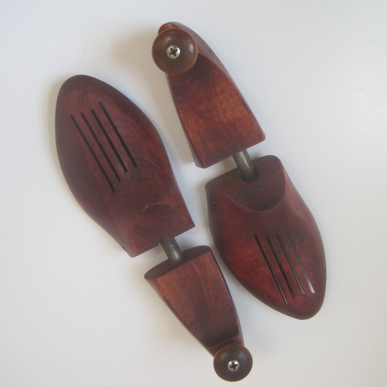 Puede incluir: Un par de hormas de zapatos de madera con un acabado marr&oacute;n rojizo oscuro. Las hormas tienen una parte superior redondeada y una varilla de metal que conecta las dos piezas.