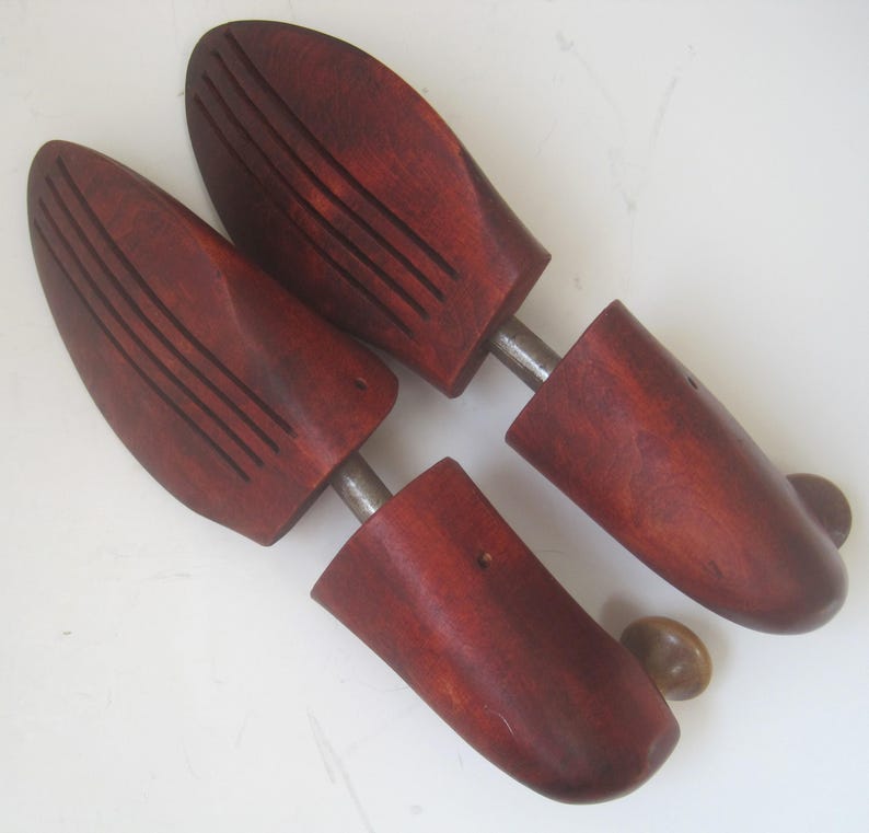 K&ouml;nnte beinhalten: Ein Paar Schuhspanner aus Holz mit einer rotbraunen Oberfl&auml;che. Die Schuhspanner haben eine Metallstange, die die beiden H&auml;lften verbindet, und einen Knopf an einem Ende.