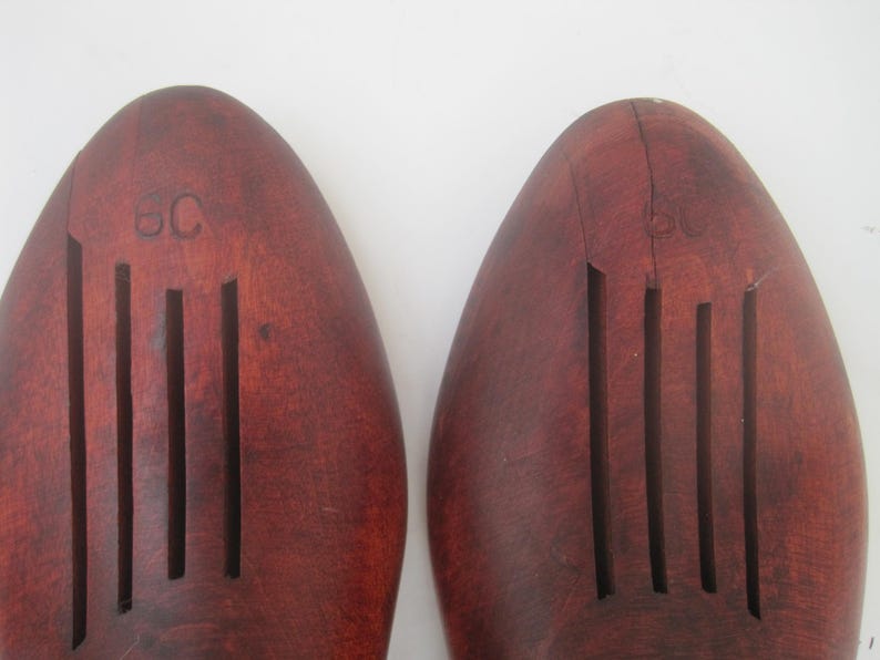 K&ouml;nnte beinhalten: Ein Paar braune Holzschuhspanner mit geriffeltem Design und dem Buchstaben "C" auf der Oberseite.