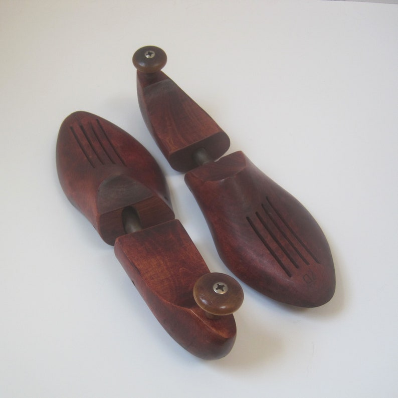 Puede incluir: Un par de hormas de zapatos de madera con un acabado marr&oacute;n rojizo oscuro. Las hormas est&aacute;n hechas de dos piezas que encajan entre s&iacute; y tienen una perilla en el extremo para ajustar el ajuste.