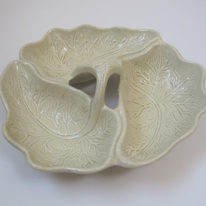 May include: A three-sectioned ceramic serving dish with a leaf design. The dish is off-white with a speckled glaze and has a handle in the center.