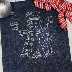May include: White embroidered design of a snowman on a dark blue denim fabric. The snowman is wearing a hat and scarf and has a small bird perched on its arm.