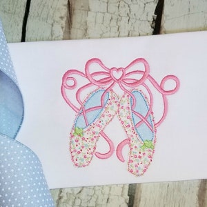 May include: Embroidered design of a pair of pink ballet shoes with a pink bow and floral print. The shoes are tied together with a ribbon.
