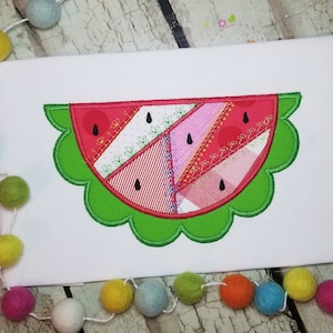 Può includere: Un'applique di anguria rossa e verde con un bordo a festoni. L'anguria è realizzata in tessuto patchwork con diversi motivi e colori.