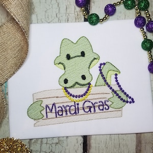 Könnte beinhalten: Grüner Alligator, der ein Schild mit der Aufschrift "Mardi Gras" hält, mit lila Perlen um den Hals.