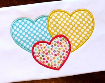 May include: Three embroidered hearts in different patterns. The largest heart is yellow with white polka dots, the middle heart is blue with white polka dots, and the smallest heart is pink with a multi-colored floral pattern.
