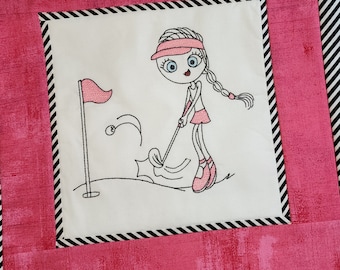May include: Embroidered design of a girl playing golf. She is wearing a pink hat, pink shirt, and pink skirt. She is holding a golf club and hitting a golf ball. There is a golf flag in the background.