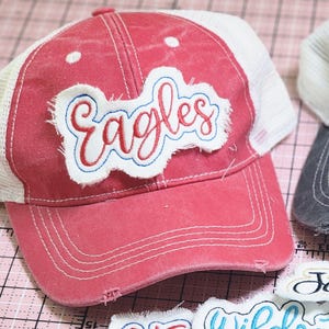 Peut inclure: Casquette de baseball rouge délavé avec un dos en filet blanc. Le mot "Eagles" est brodé en rouge avec un contour bleu sur un écusson blanc. Aspect vieilli.