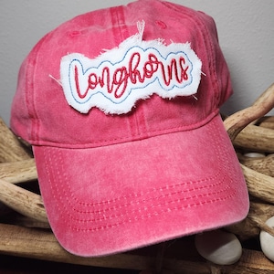 May include: A faded red baseball cap with the word "Longhorns" embroidered on a white patch. The text is in red script with a blue outline. The hat has a curved brim and a distressed look.