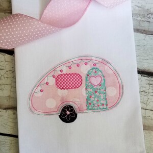 Op de afbeelding: Roze en witte camper met witte stippen, een groene en witte bloemen deur en een roze en wit geruit raam. De camper heeft een zwart wiel met een witte bloem.