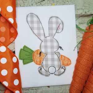 May include: A gray and white checkered bunny holding a carrot. The bunny is facing away from the viewer and has a small pink nose. The carrot is green at the top and orange at the bottom.