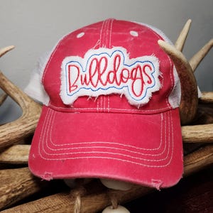 Pode incluir: Boné de caminhoneiro vermelho e branco com um remendo branco que diz "Bulldogs" em bordado vermelho e azul.