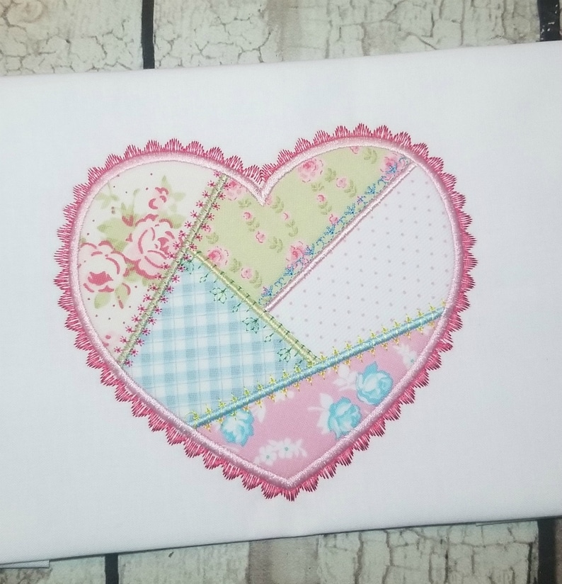 May include: A pink heart-shaped patch with a patchwork design. The patch is made of different fabrics with floral, checkered, and polka dot patterns. The heart is outlined with a pink scalloped edge.